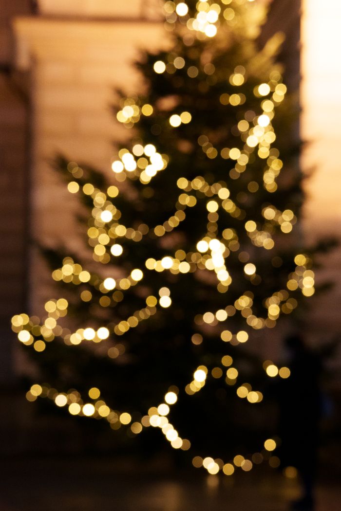 Blurred view of a Christmas tree adorned with glowing lights in a nighttime setting.