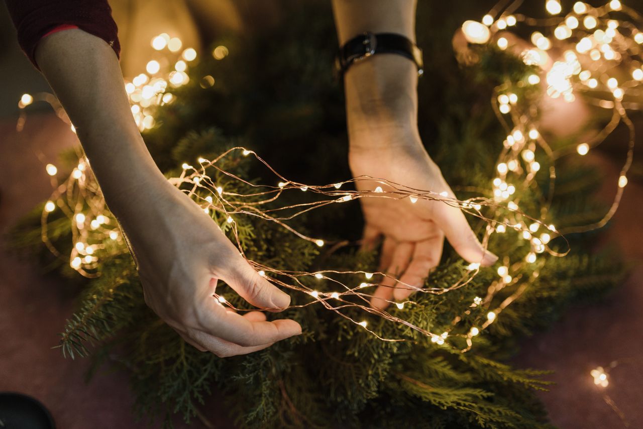Close-up of hands decorating a Christmas wreath with glowing fairy lights for a festive touch.